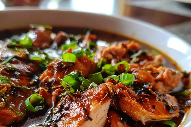 Chicken thighs browning in a Dutch oven with golden caramelized sugar and aromatic spices visible in the background, steam rising from the pan