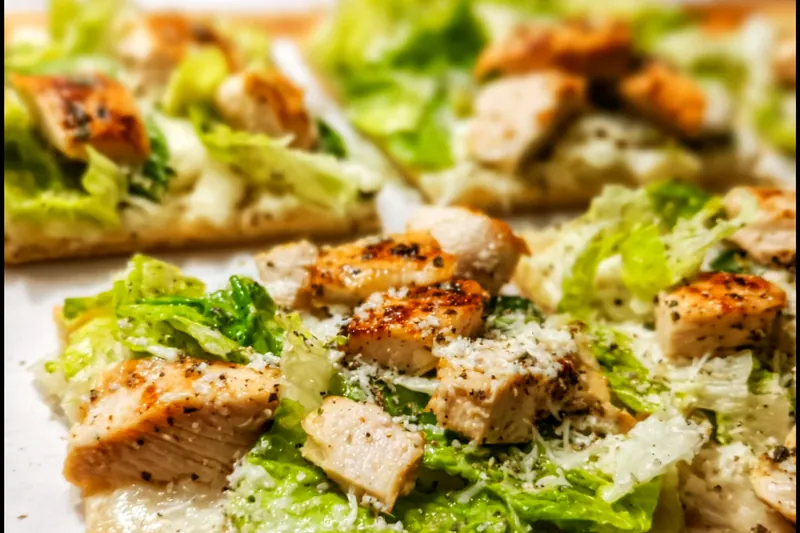 Ingredients for chicken Caesar flatbread including flatbread, grilled chicken, romaine lettuce, Parmesan cheese, and Caesar dressing ingredients