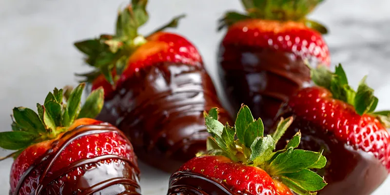 A close-up of chocolate-covered cheesecake strawberries on a white plate
