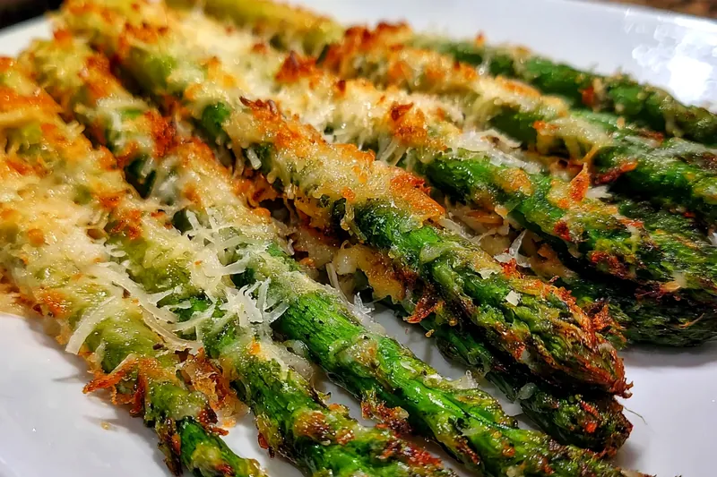 Step-by-step process showing asparagus being coated in flour, egg, and cheese-breadcrumb mixture before being arranged on a parchment-lined baking sheet